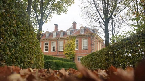 A view of Hanbury Hall framed by autumn leaves on the ground